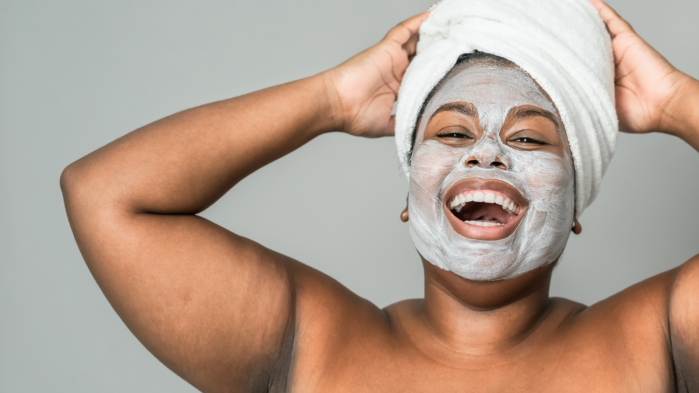 mulher negra feliz realizando skin care com tolha na cabeça